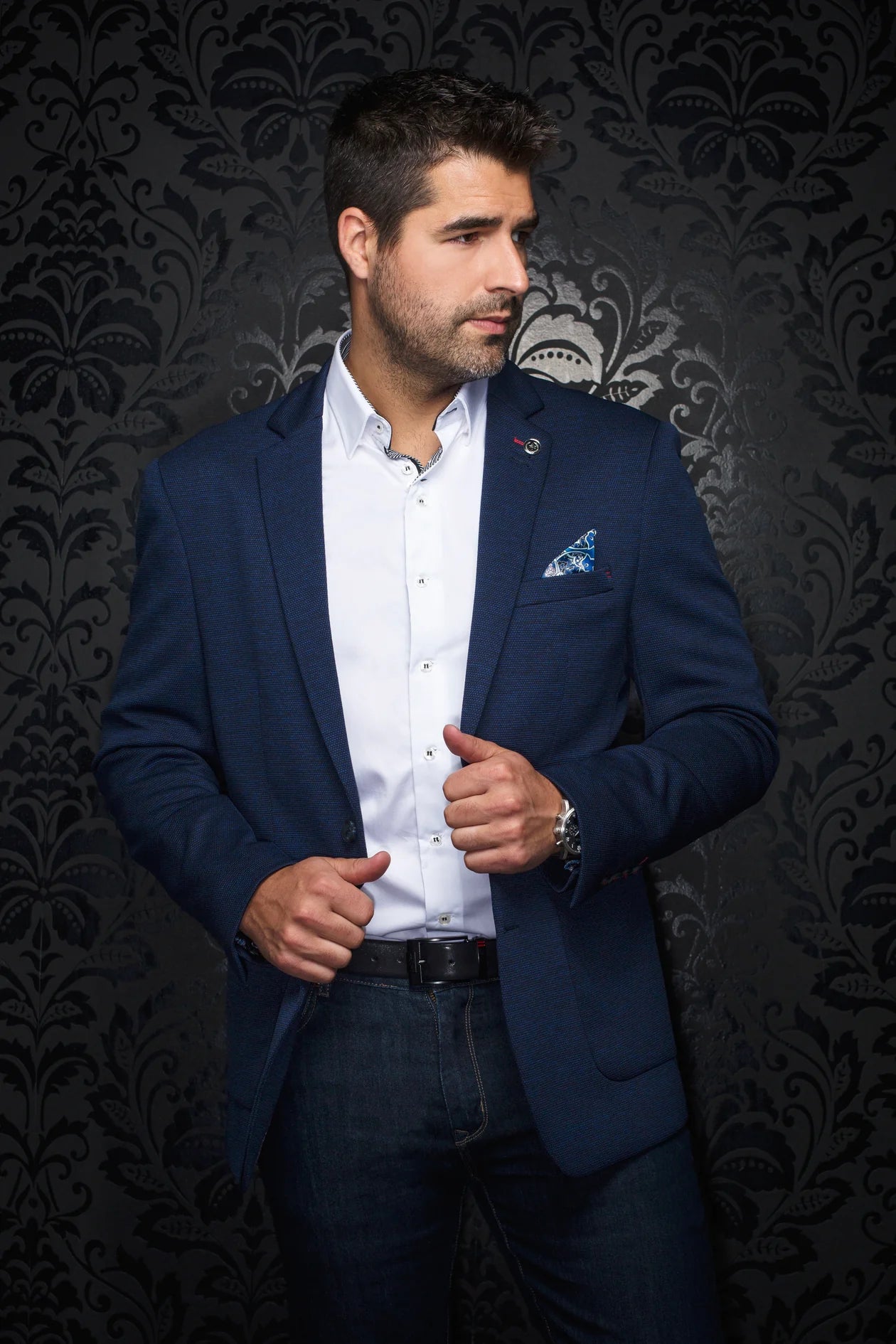 Man wearing a blue blazer over a white shirt with a patterned dark background