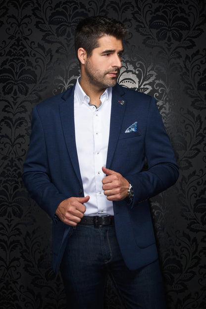 Man wearing a blue blazer over a white shirt with a patterned dark background