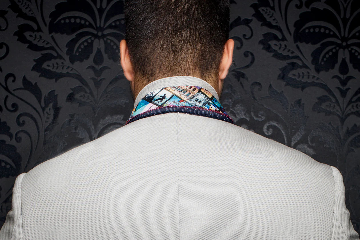 Person wearing a light gray suit with a colorful tie against a dark patterned wall.