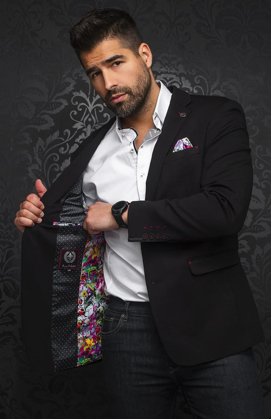 Man wearing a black blazer with floral tie and patterned pocket square against a dark background