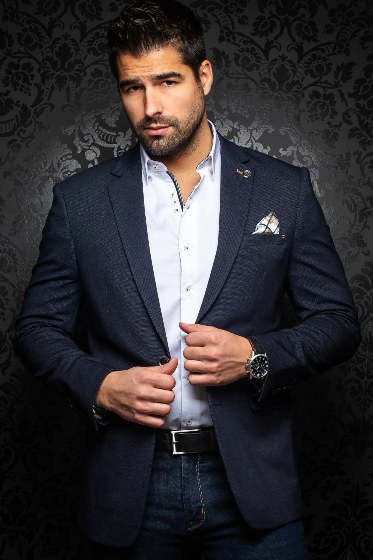 Man wearing a navy blazer over a light shirt with a dark background