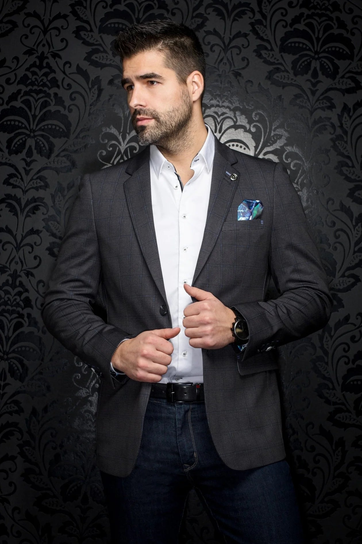 Man wearing a dark blazer over a white shirt with a patterned background