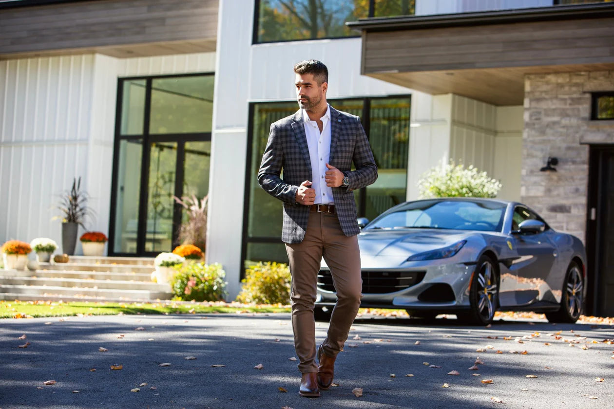 Man in formal attire walking in front of a modern house with a car in the background