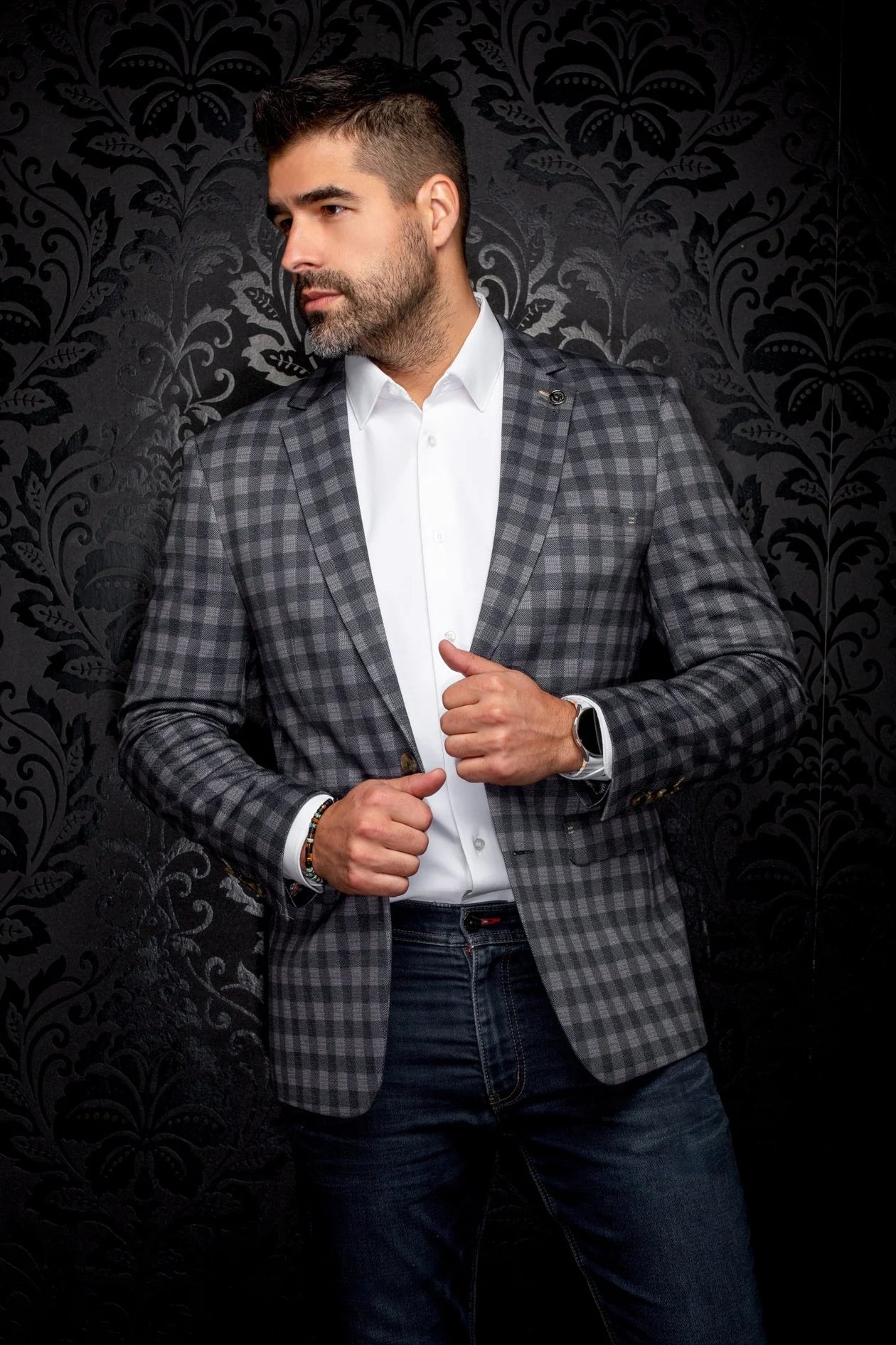Man wearing a checkered blazer over a white shirt against a dark patterned background
