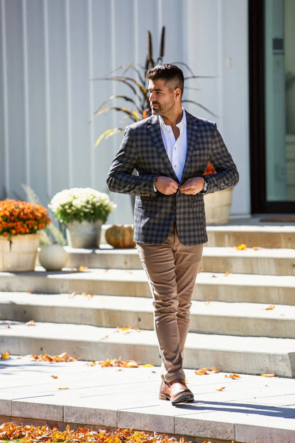 Man in a plaid blazer and beige pants walking outdoors on steps.