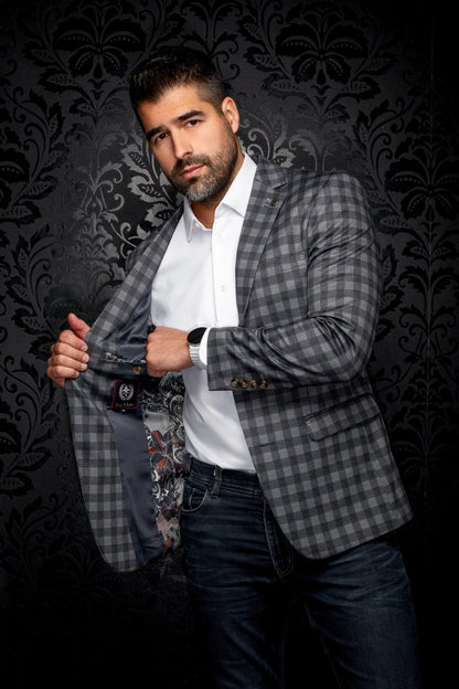 Man wearing a checkered blazer over a white shirt with a patterned tie against a dark, decorative background.