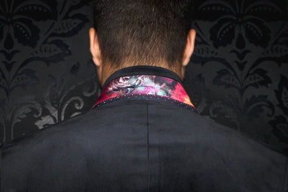 Person wearing a dark coat with a colorful collar against a dark patterned background