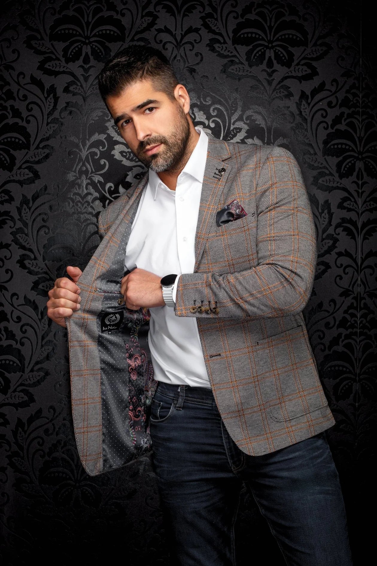 Man wearing a patterned blazer over a white shirt with a dark background