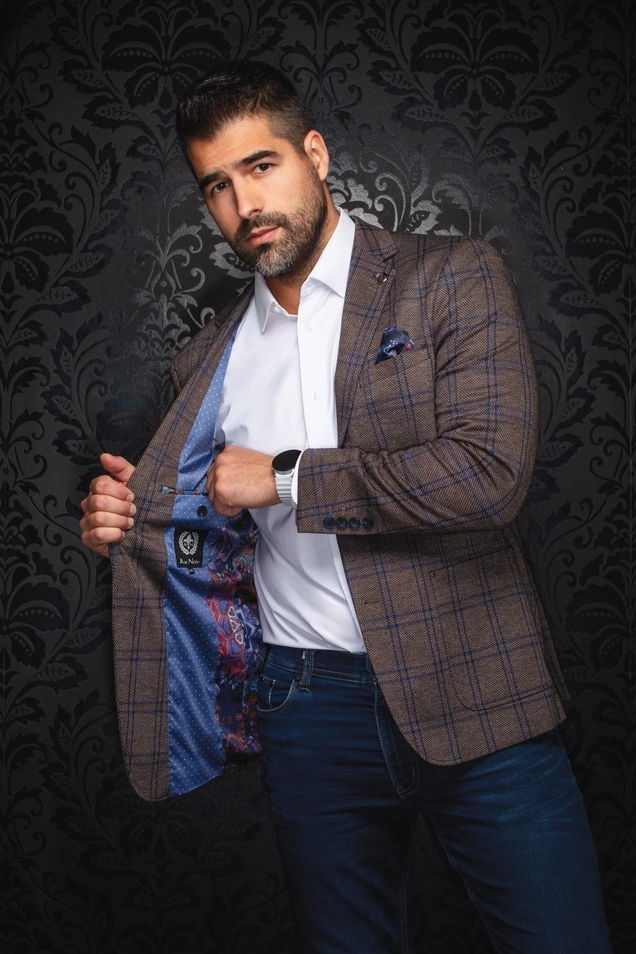 Man wearing a brown checkered blazer over a white shirt with a dark patterned background