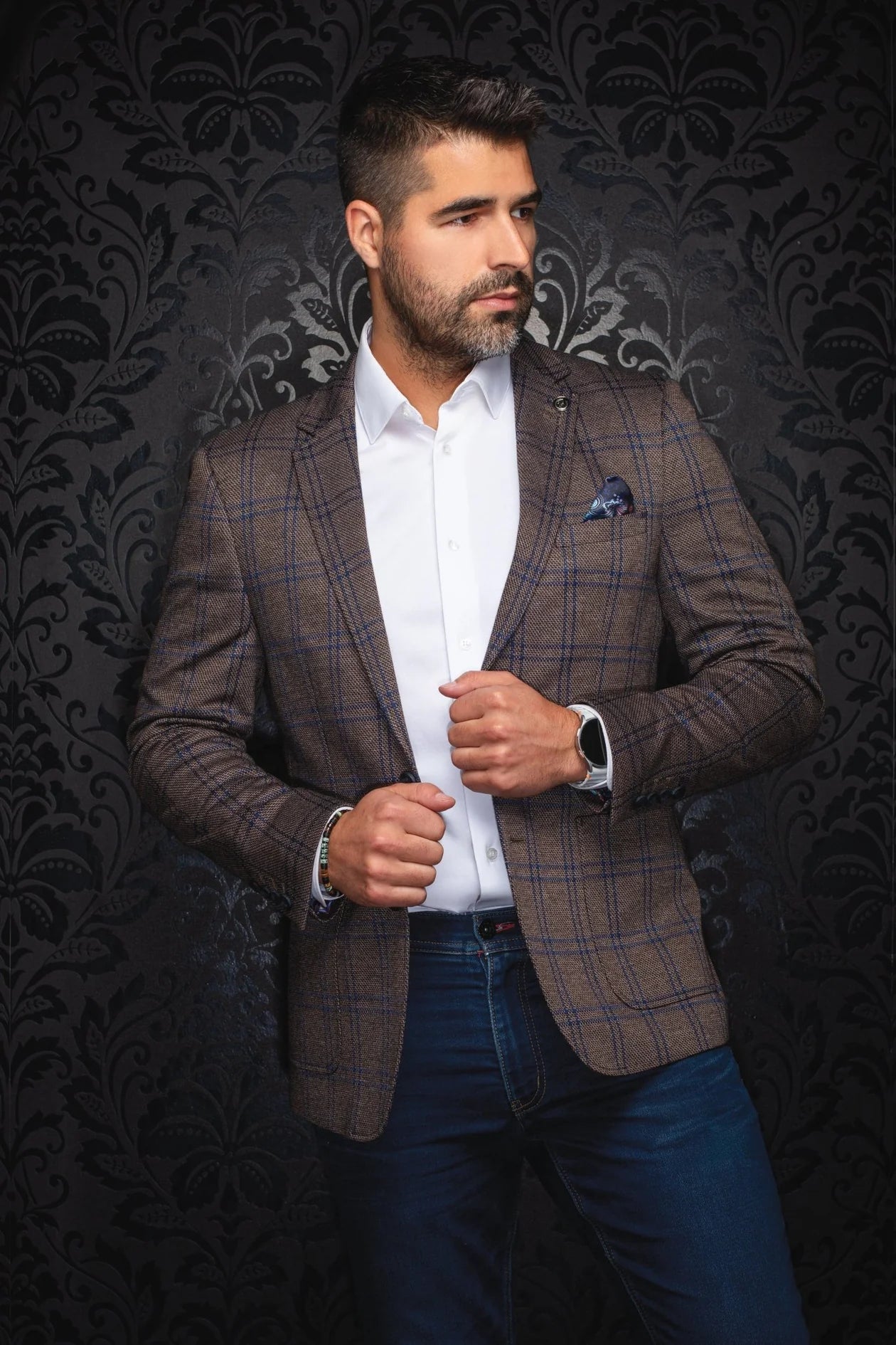 Man wearing a brown checkered blazer over a white shirt with a dark patterned background