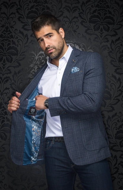 Man wearing a blue checkered blazer over a white shirt with a floral pocket square, against a dark patterned wall.