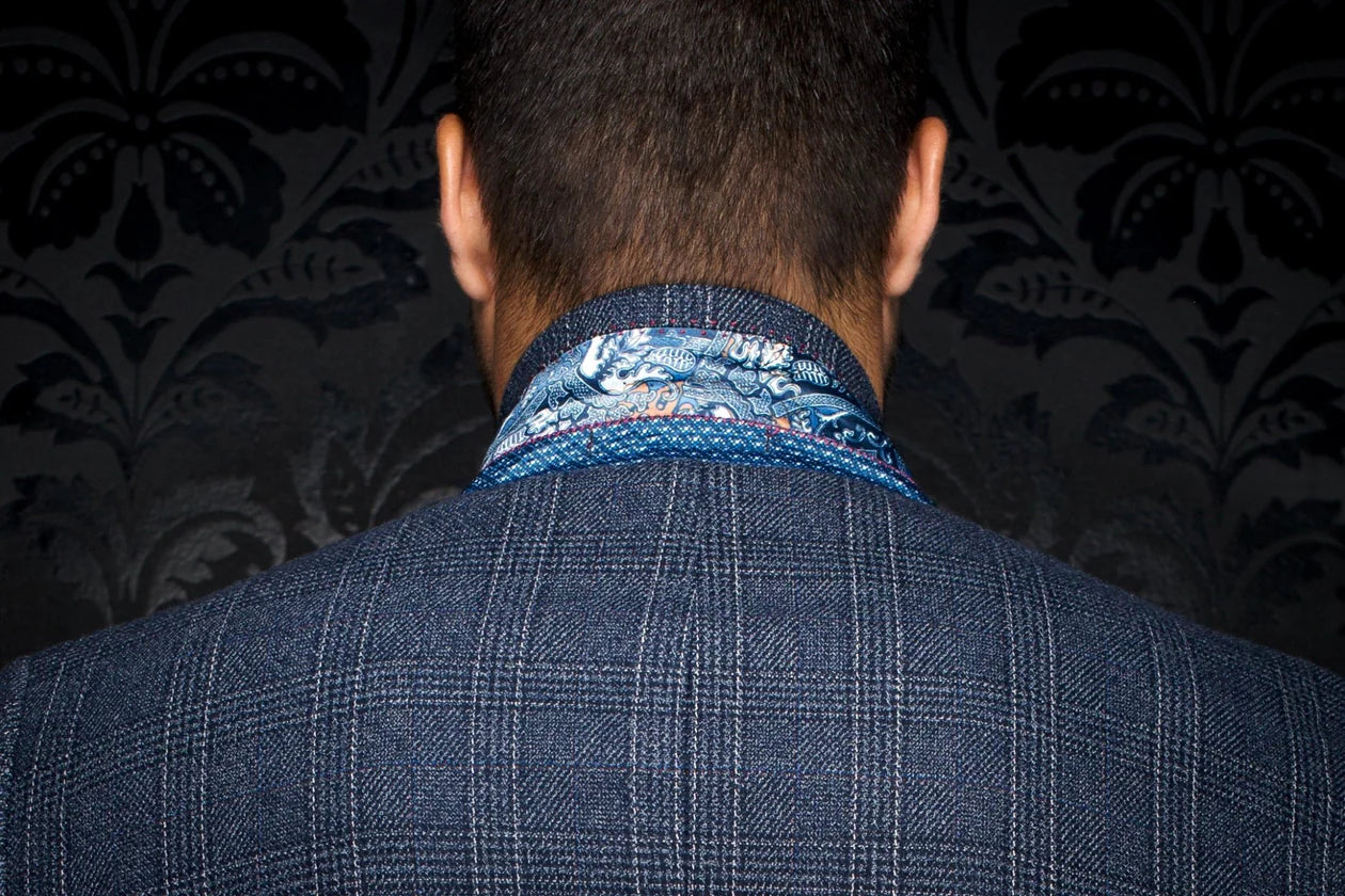 Person wearing a blue checkered suit with a patterned shirt collar against a dark background