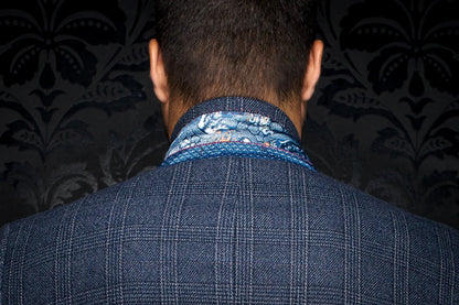 Person wearing a blue checkered suit with a patterned shirt collar against a dark background