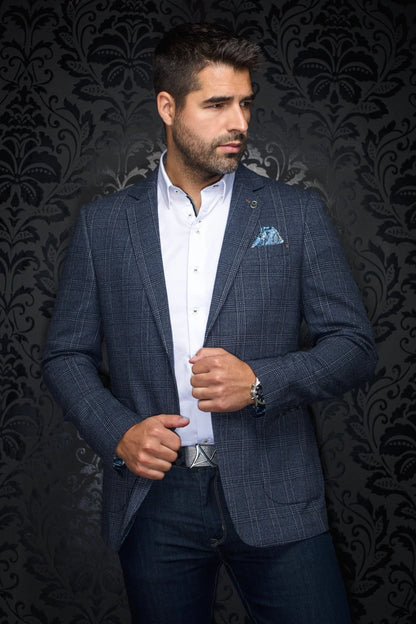 Man wearing a blue checkered suit with a white shirt and patterned pocket square against a dark, decorative wall.