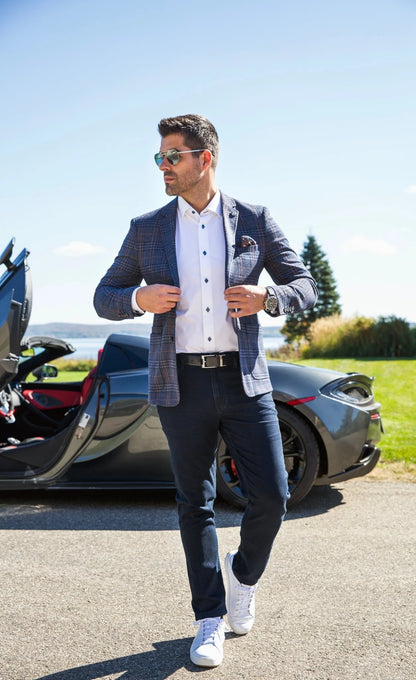 Man in formal attire standing next to a sports car on a sunny day