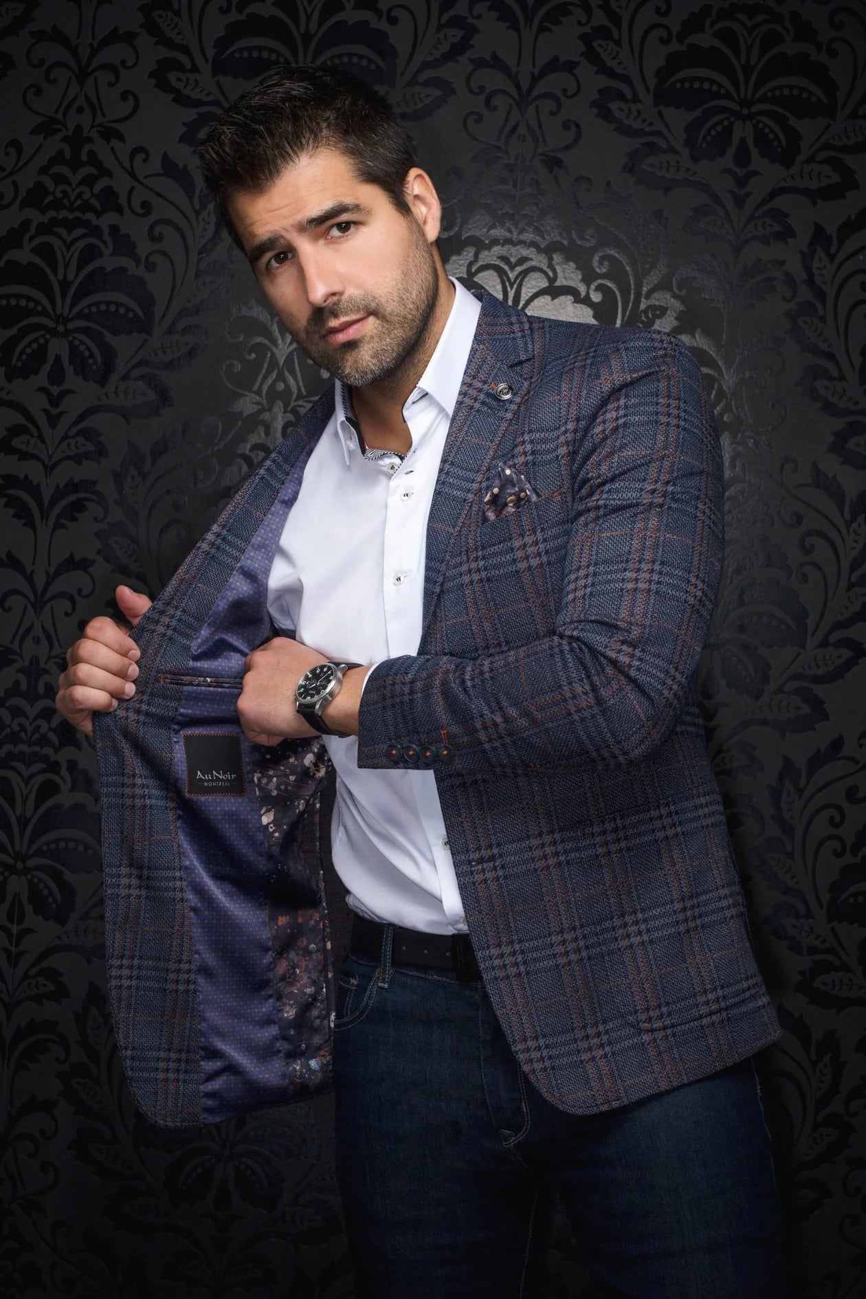 Man wearing a plaid blazer over a white shirt against a dark patterned background