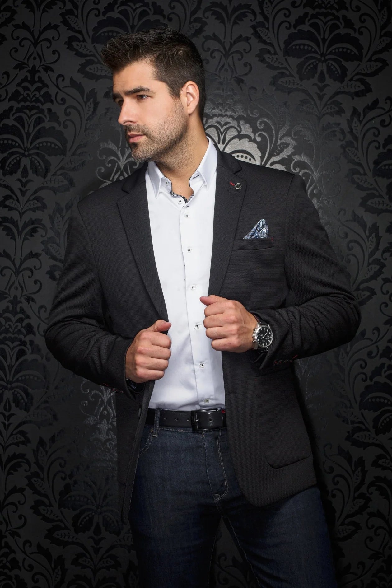 Man wearing a black blazer over a white shirt with a decorative background