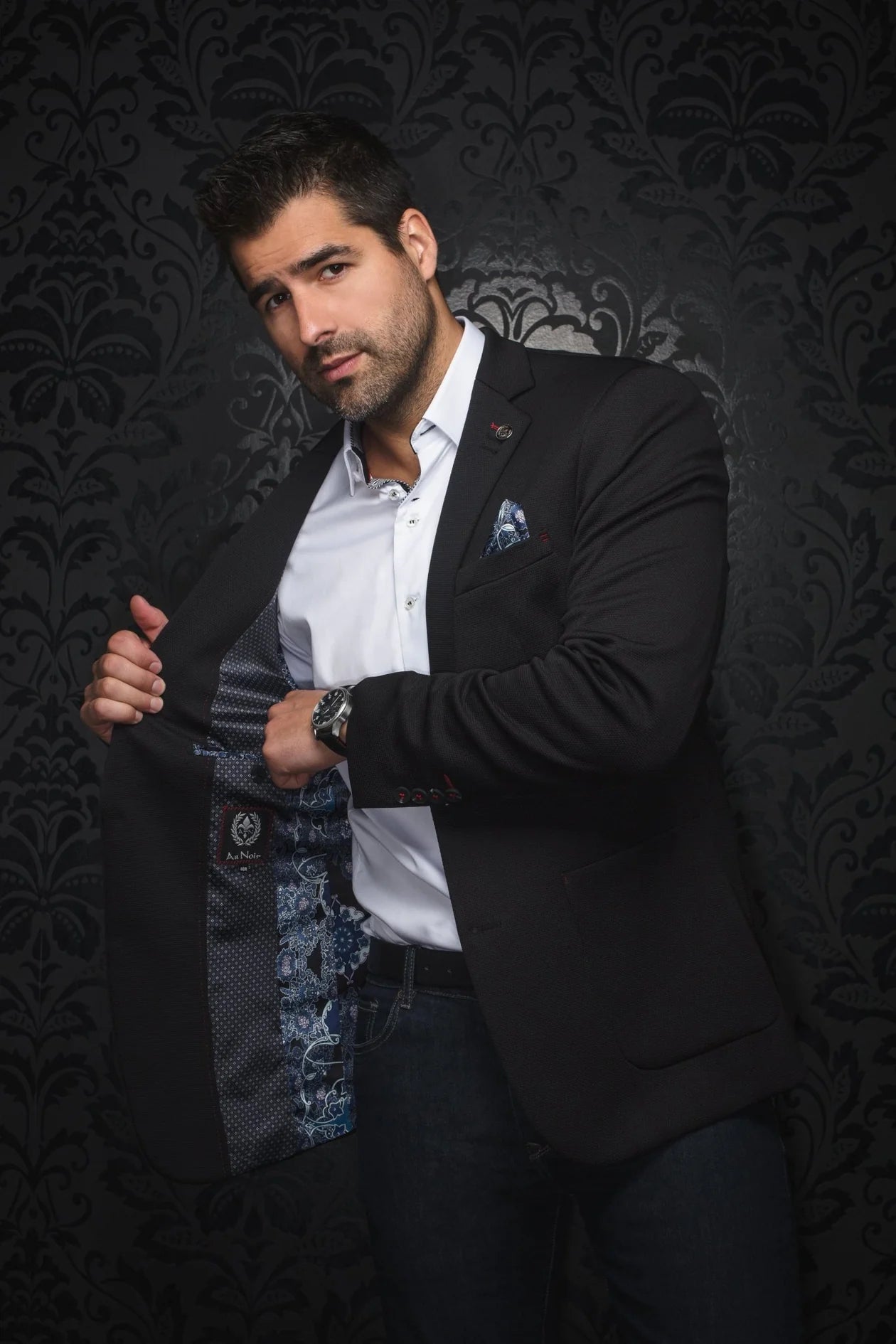 Man adjusting his jacket against a dark, patterned background
