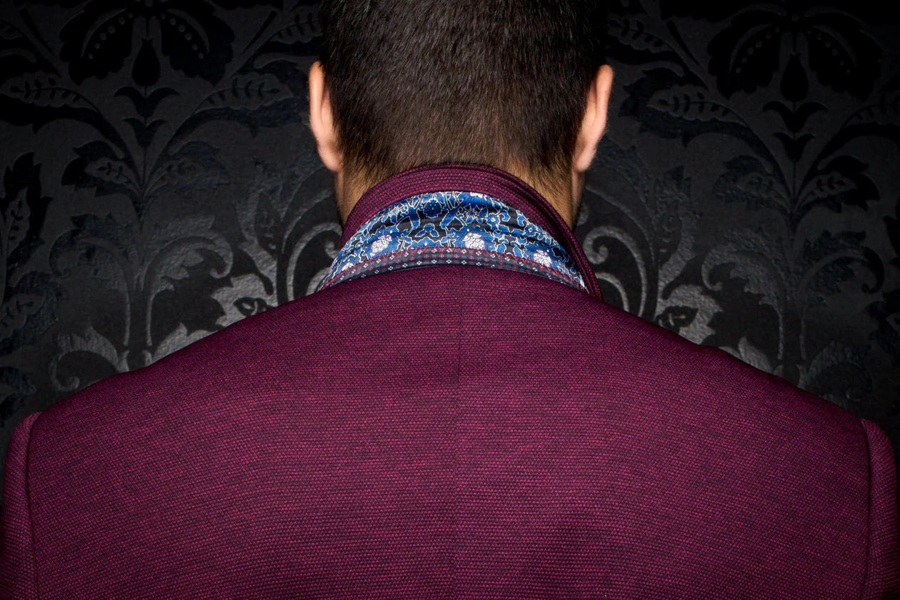 Back view of a person wearing a patterned shirt and maroon jacket against a dark, decorative wall.