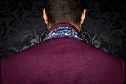 Back view of a person wearing a patterned shirt and maroon jacket against a dark, decorative wall.