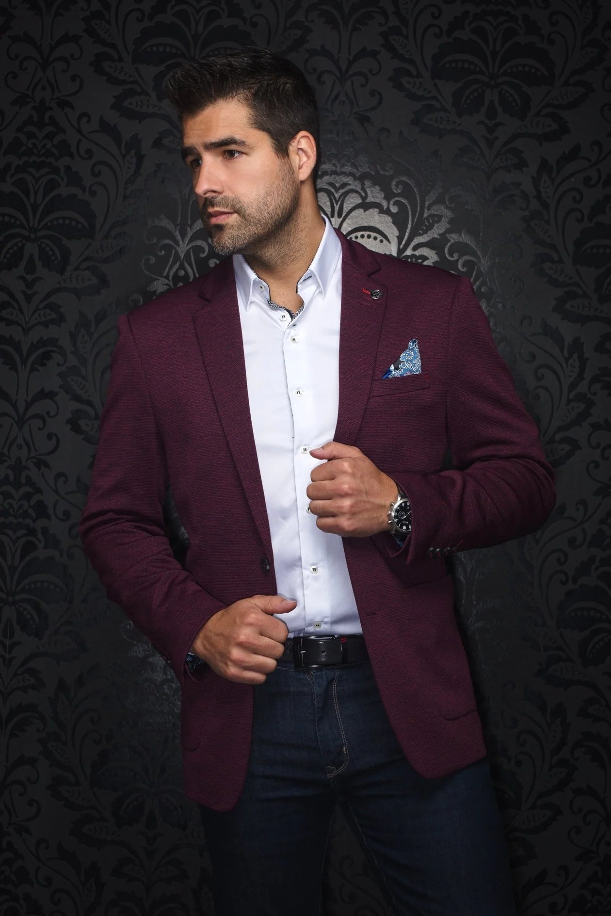 Man wearing a burgundy blazer over a white shirt with a dark background