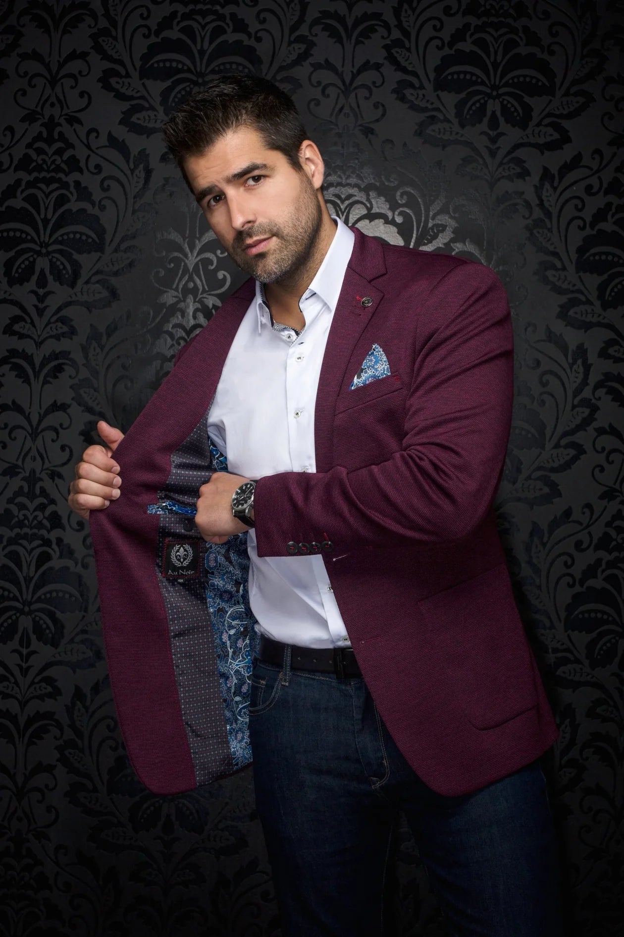 Man wearing a burgundy blazer over a white shirt with a patterned background