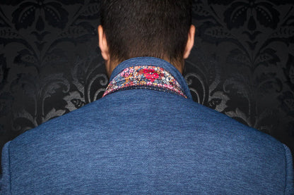 Back view of a person wearing a blue jacket with a patterned collar against a dark, decorative background.