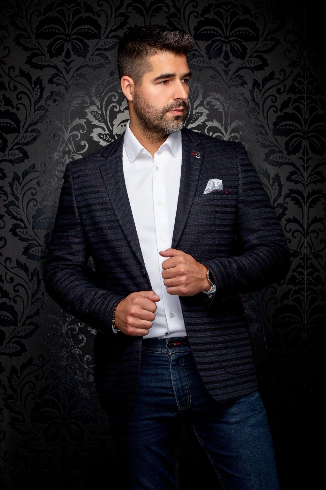 Man wearing a dark blazer over a white shirt with a patterned background