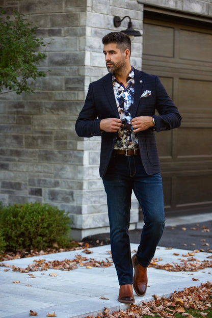 Man in a suit and floral shirt standing outdoors near a building.