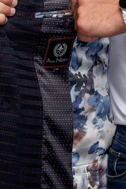 Close-up of a patterned tie with 'Au Noir' branding held by a person wearing a floral shirt.
