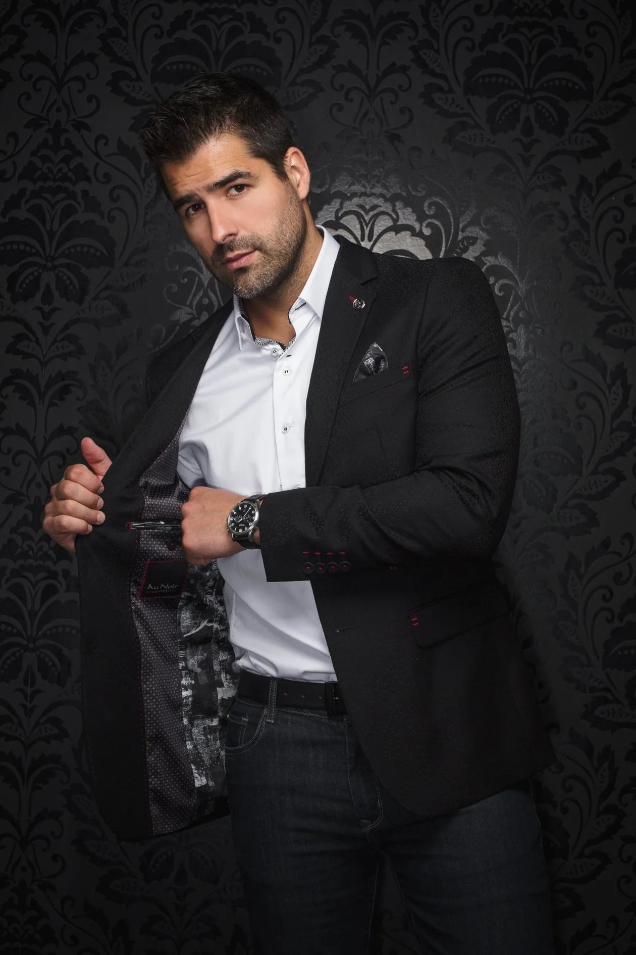 Man wearing a black blazer over a white shirt with a decorative background