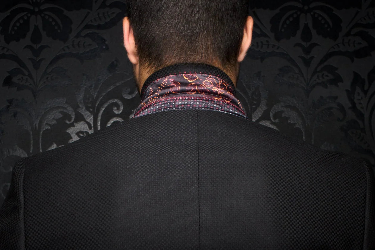 Person wearing a dark suit with a patterned shirt collar against a dark, textured wall.