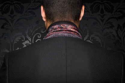 Person wearing a dark suit with a patterned shirt collar against a dark, textured wall.