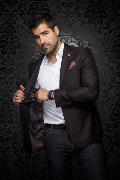 Man adjusting his jacket against a dark, patterned background