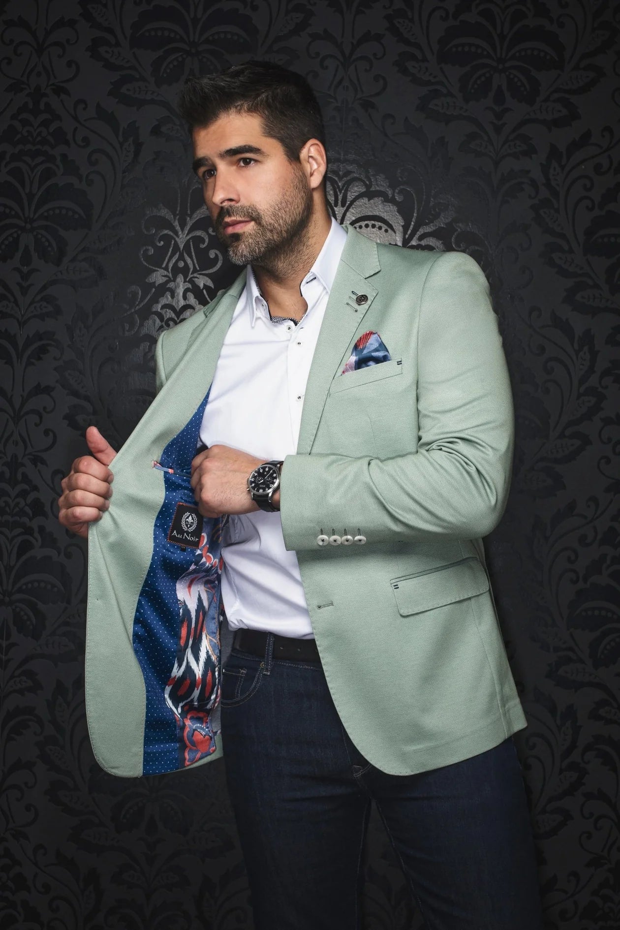 Man wearing a light green blazer with a patterned tie against a dark background