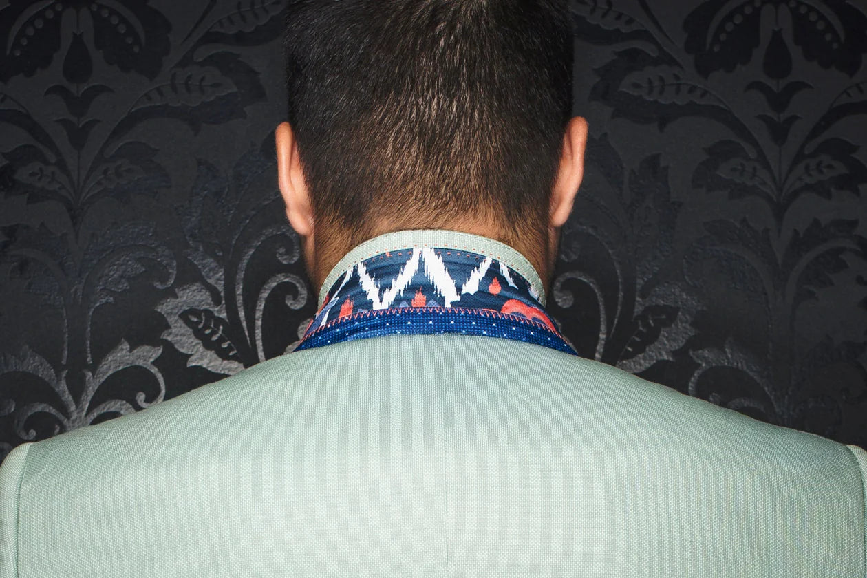 Person wearing a patterned necktie with a dark floral-patterned wall in the background