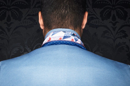 Back view of a person wearing a blue suit with a patterned shirt collar against a dark floral wallpaper.