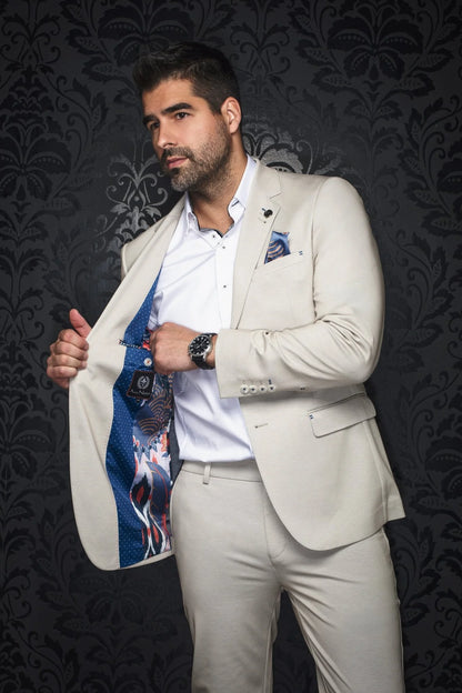 Man in a light-colored suit with a patterned shirt against a dark, decorative wall.