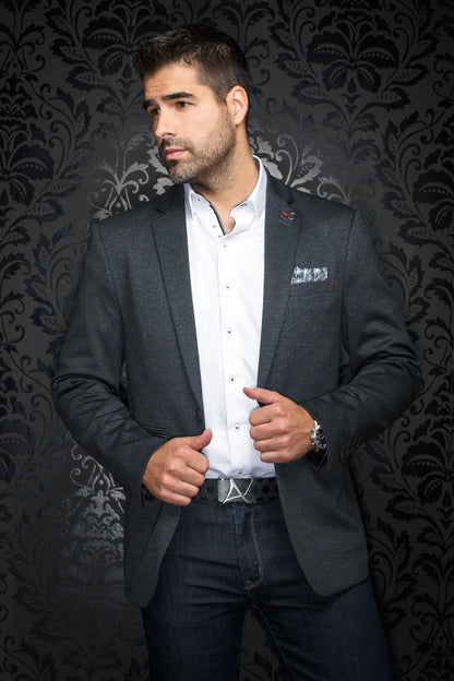Man wearing a dark blazer over a white shirt with a patterned background