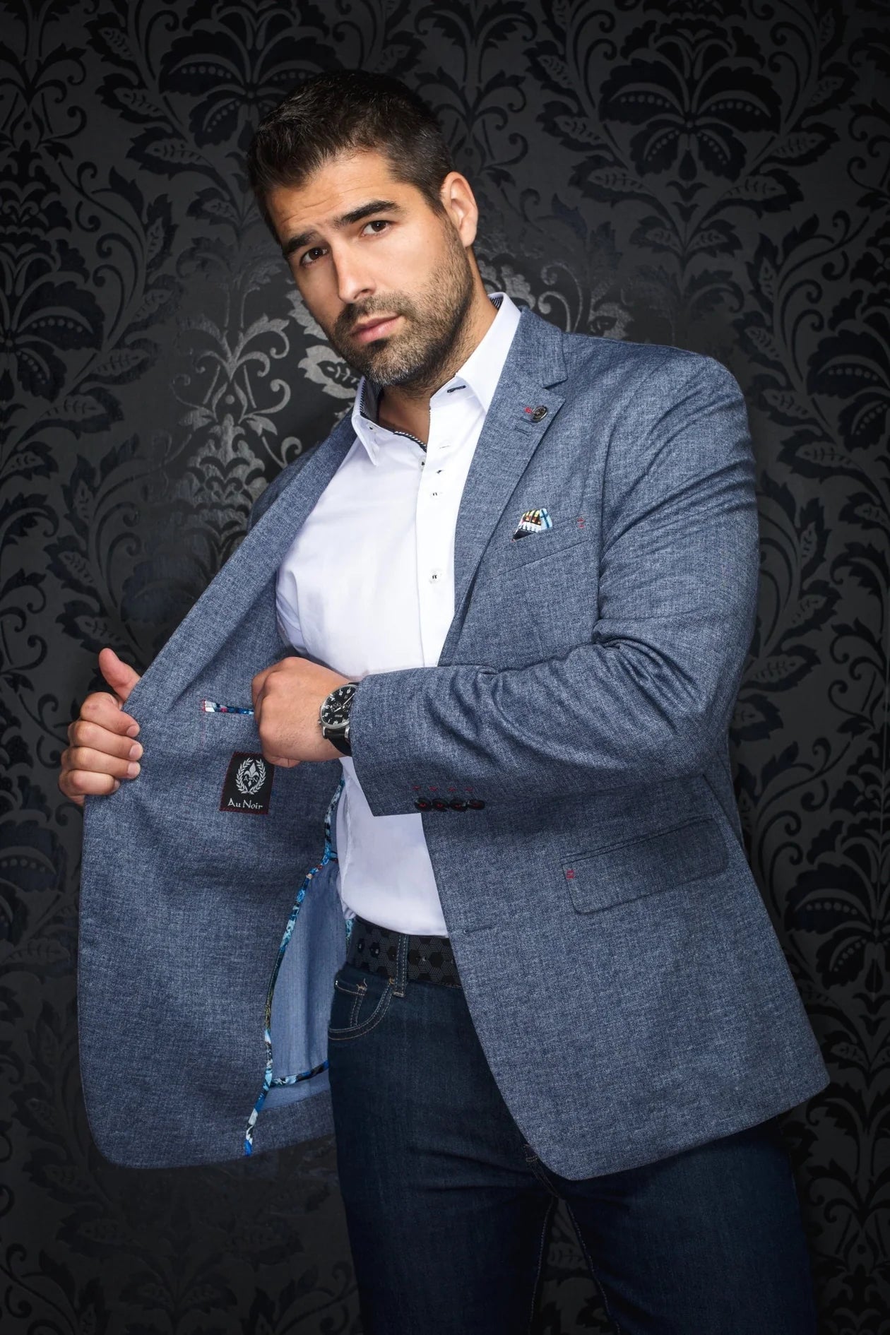 Man wearing a gray blazer over a white shirt with a dark patterned background