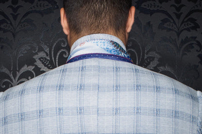 Back view of a person wearing a blue checkered suit jacket with a patterned shirt underneath against a dark floral wallpaper.