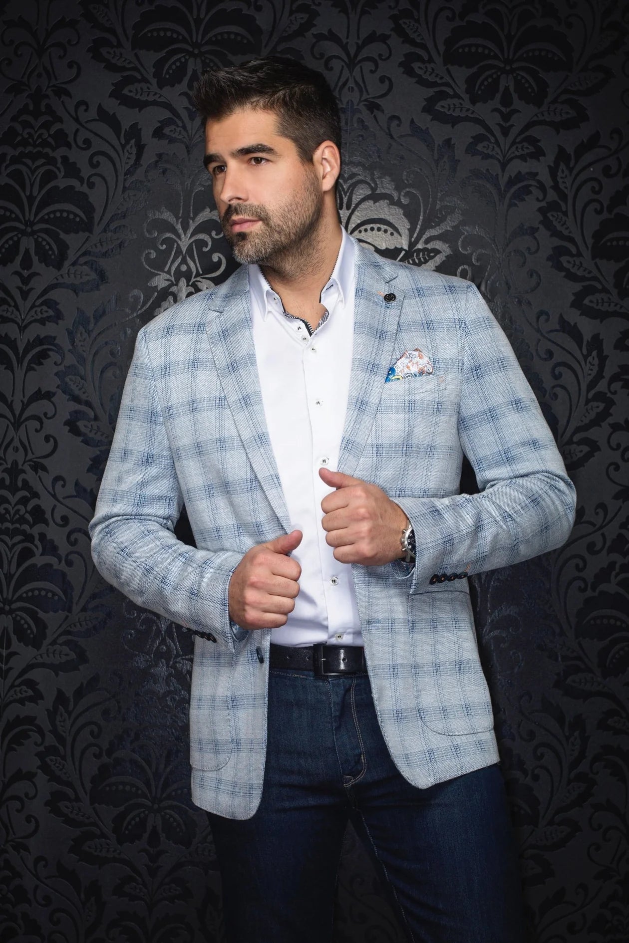 Man wearing a light blue checkered blazer over a white shirt with a dark background