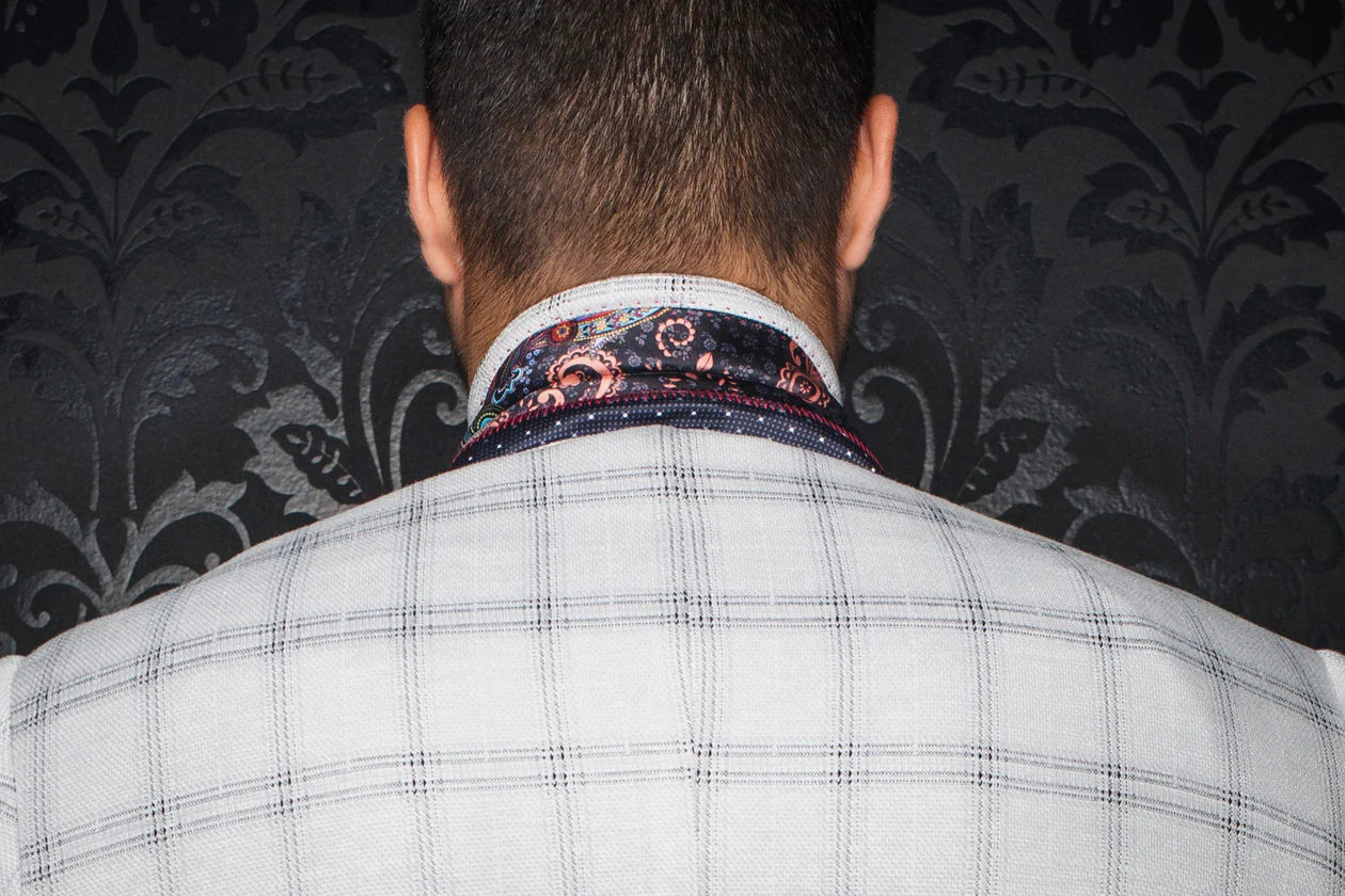 Person wearing a checkered suit jacket with a patterned shirt collar against a dark floral wallpaper background