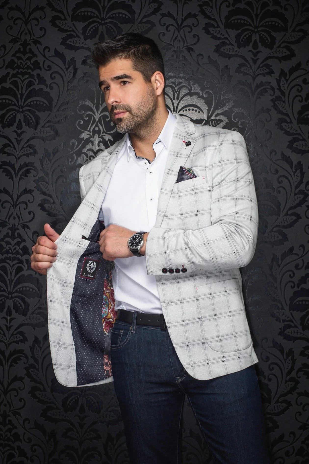 Man wearing a light gray checkered blazer over a white shirt with a dark background