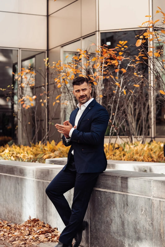 Man in a dark suit sitting on a ledge with autumn leaves and modern building in the background
