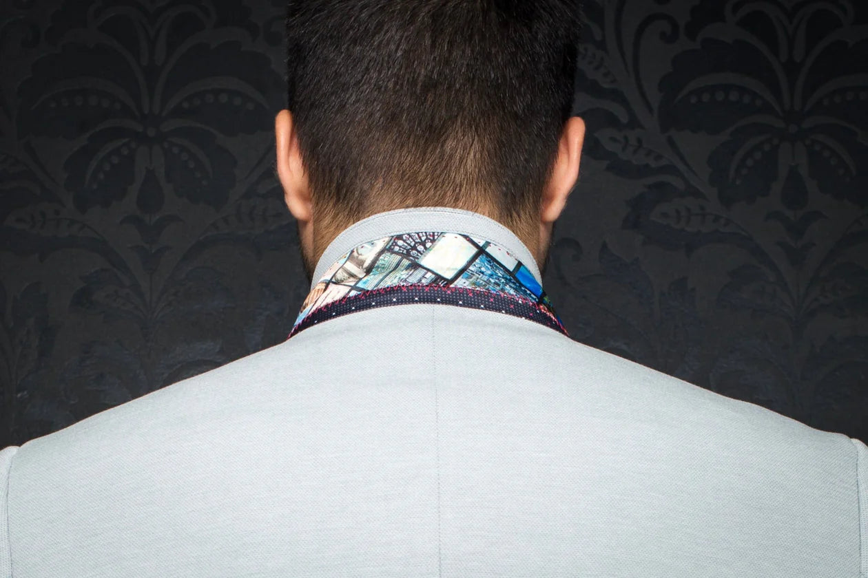 Person wearing a light gray suit with a patterned tie against a dark, textured wall.