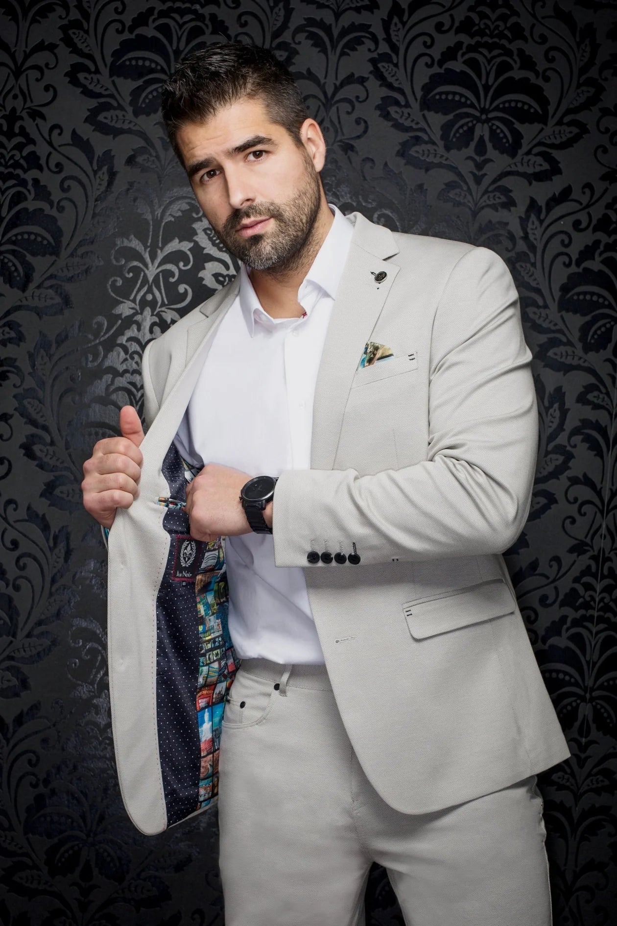 Man in a light gray suit with a patterned tie against a dark, decorative background