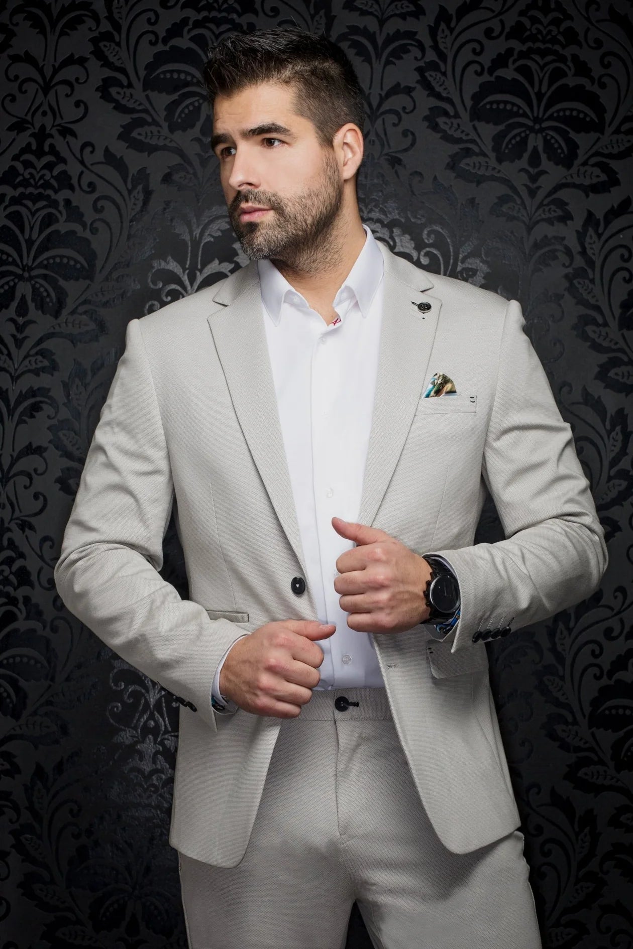 Man wearing a light gray suit with a white shirt against a dark patterned background